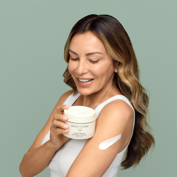 Woman with cream on arm holding Body Firm Advanced Body Care Treatment from Crepe Erase